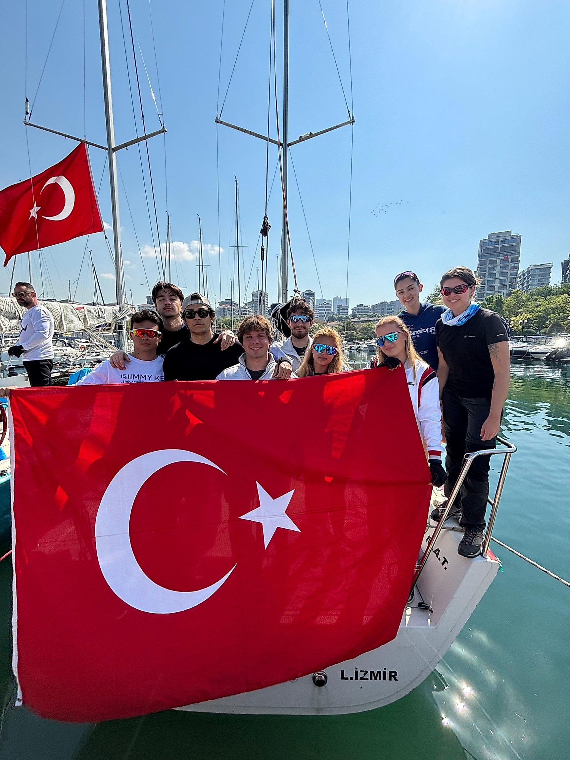 Marinada bir teknenin kıçında büyük bir Türk bayrağı tutan güneş gözlüklü ekip.